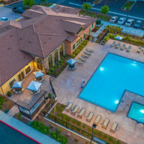 Elk Grove, CA Apartments - Vasari - Aerial View of Pool with Lounge Chairs, Tables, Umbrellas, Patio Sets, Maintained Landscaping, and Resident Lounge